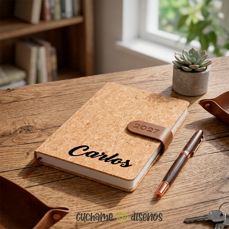 Agenda de corcho personalizada con nombre en un escritorio de madera junto a un bolígrafo y una planta